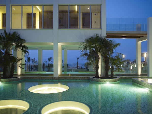 A modern hotel with a pool area, palm trees, and a view of the ocean.