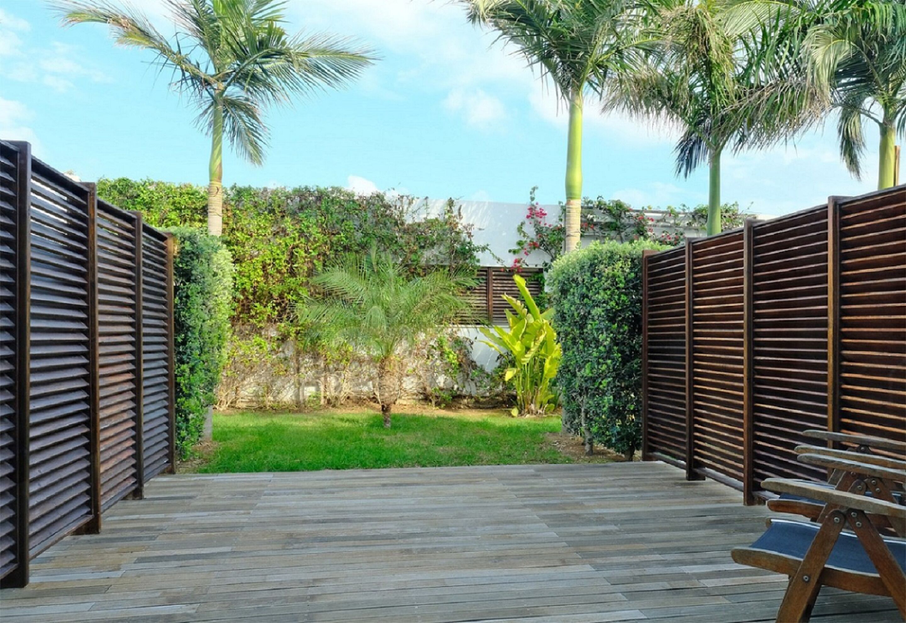 A wooden deck with a bench, surrounded by a wooden fence and tropical plants.