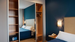 Habitación de hotel con cama, mesita de noche con teléfono, armario y luz de pared.
