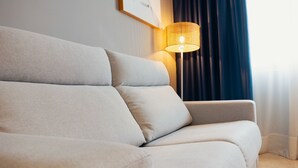 Una sala de estar moderna con un sofá color crema, una lámpara de pared y una ventana con cortinas oscuras.