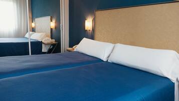 Une chambre d’hôtel avec deux lits, chacun recouvert d’une couverture bleue et doté d’oreillers blancs. Il y a une table de chevet avec une lampe et un téléphone.