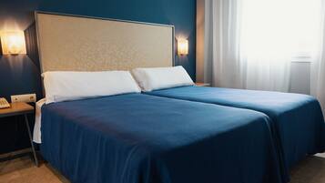 A hotel room with two beds, a nightstand with a phone, and wall-mounted lights.