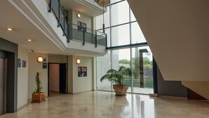 Un vestíbulo amplio con techo alto, una escalera y ventanas grandes que ofrecen vistas al exterior.