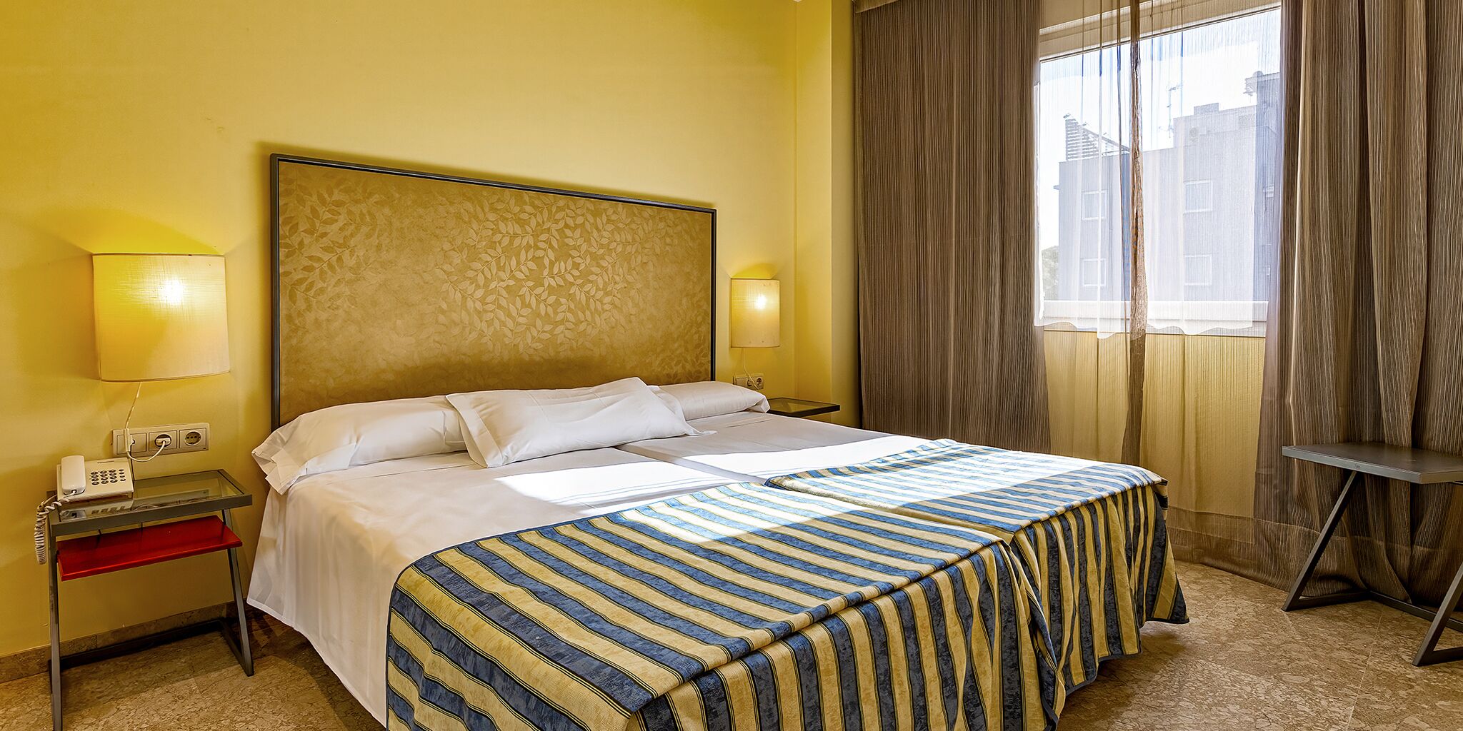 Ein Hotelzimmer mit Bett, Nachttischen, Telefon und einem Fenster mit Vorhängen.