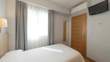 A hotel room with a bed, a flat-screen TV mounted on the wall, a wooden door, and a window with curtains.