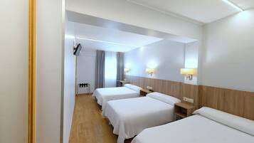 Habitació d'hotel amb tres llits individuals, un capçal de llit de fusta, taules de nit amb làmpades, un televisor de pantalla plana i una finestra amb cortines.