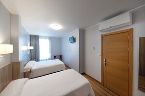 Une chambre d’hôtel avec deux lits, une armoire en bois, une télévision et une fenêtre avec des rideaux.