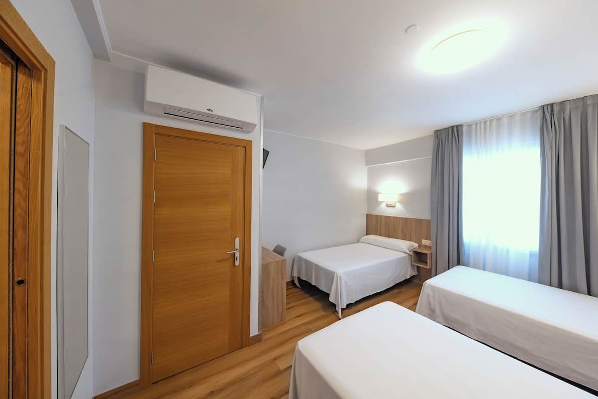 A hotel room with two single beds, a wooden wardrobe, a bedside table, a nightstand, a wall-mounted air conditioner, and a window with curtains.