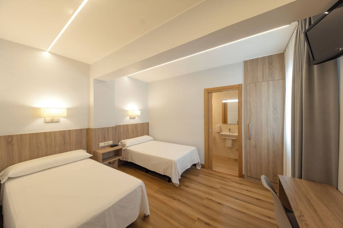 A hotel room with two beds, wooden flooring, a TV, and a wooden wardrobe.