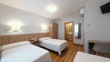 A hotel room with two single beds, a desk, a chair, a TV, and a bathroom visible through an open door.