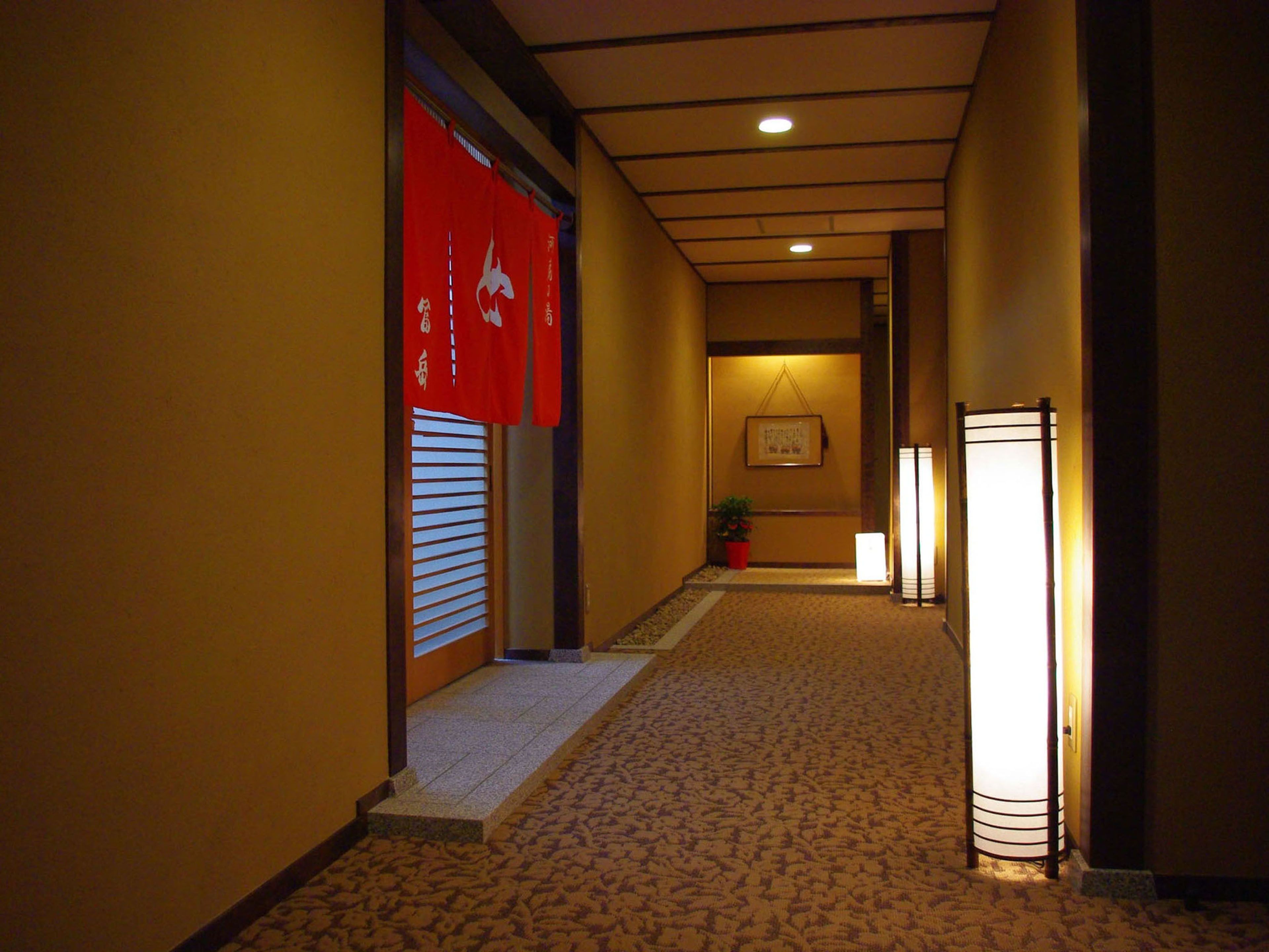 A hallway with a carpeted floor, red banners, a framed picture on the wall, and a floor lamp.