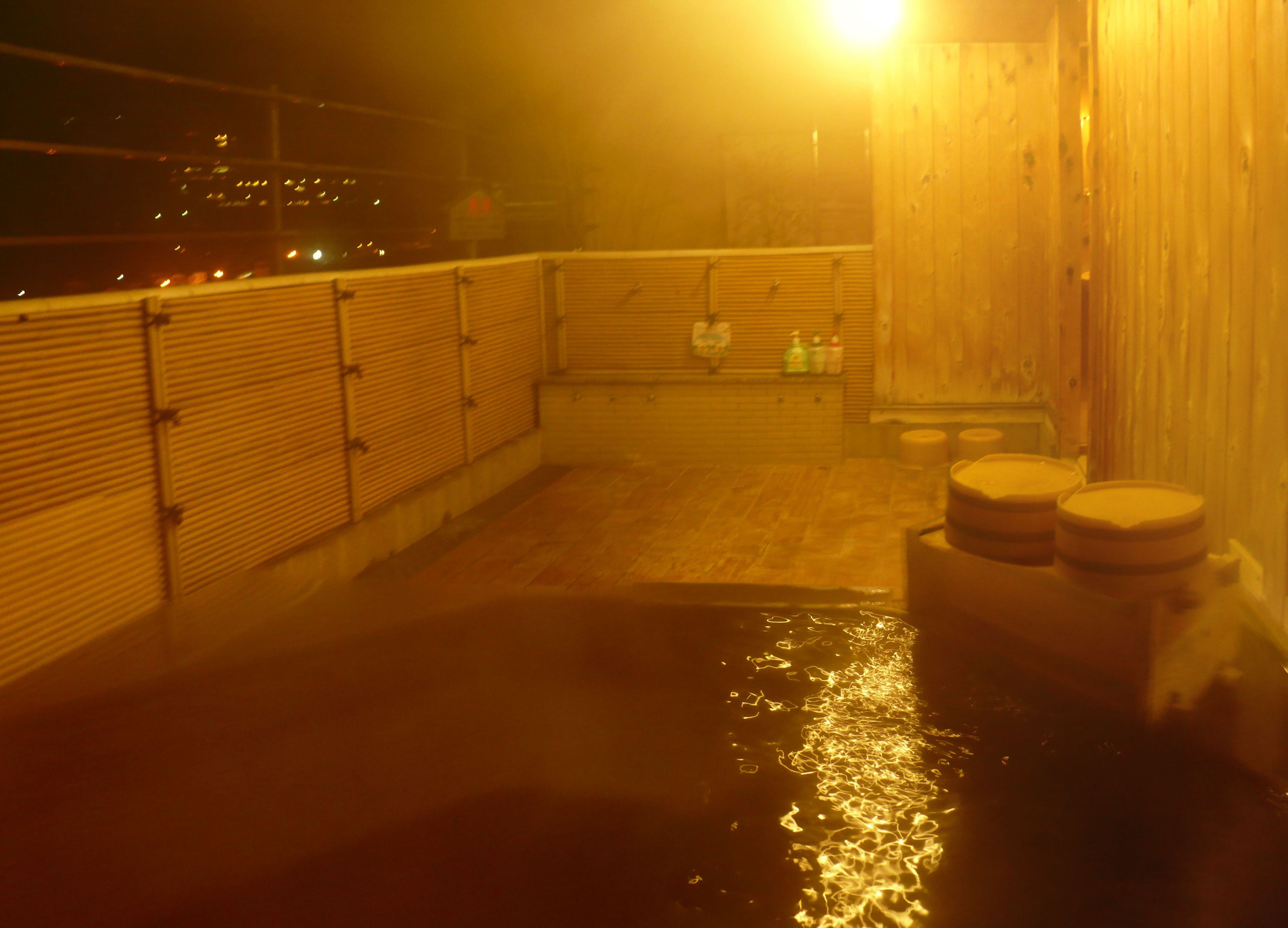 Un espace de baignade dans une source thermale, avec des bancs en bois et un sol carrelé.