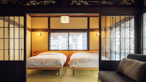 Una habitación japonesa tradicional con suelo de tatami, dos camas, un sofá y puertas correderas con paneles shoji.