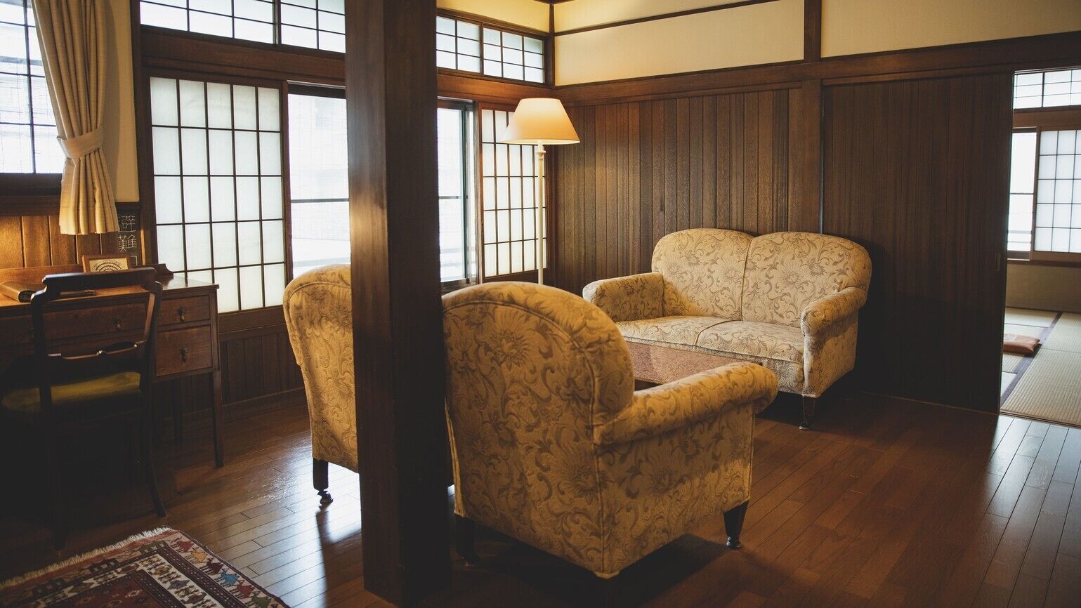 A traditional room with tatami flooring, a sofa, a desk, and a lamp.