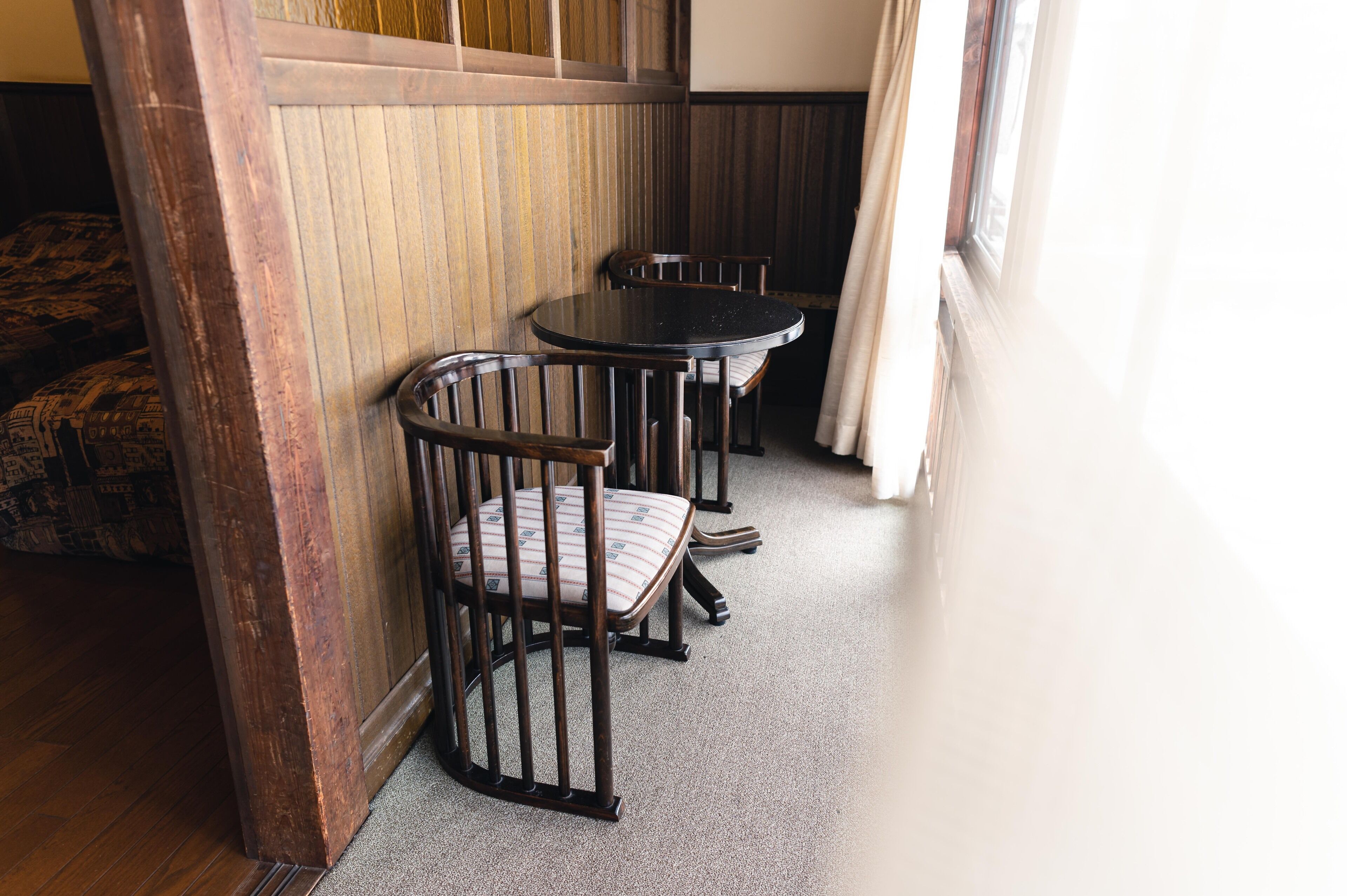 A corner of a room with a wooden wall, a window with curtains, and a carpeted floor.
