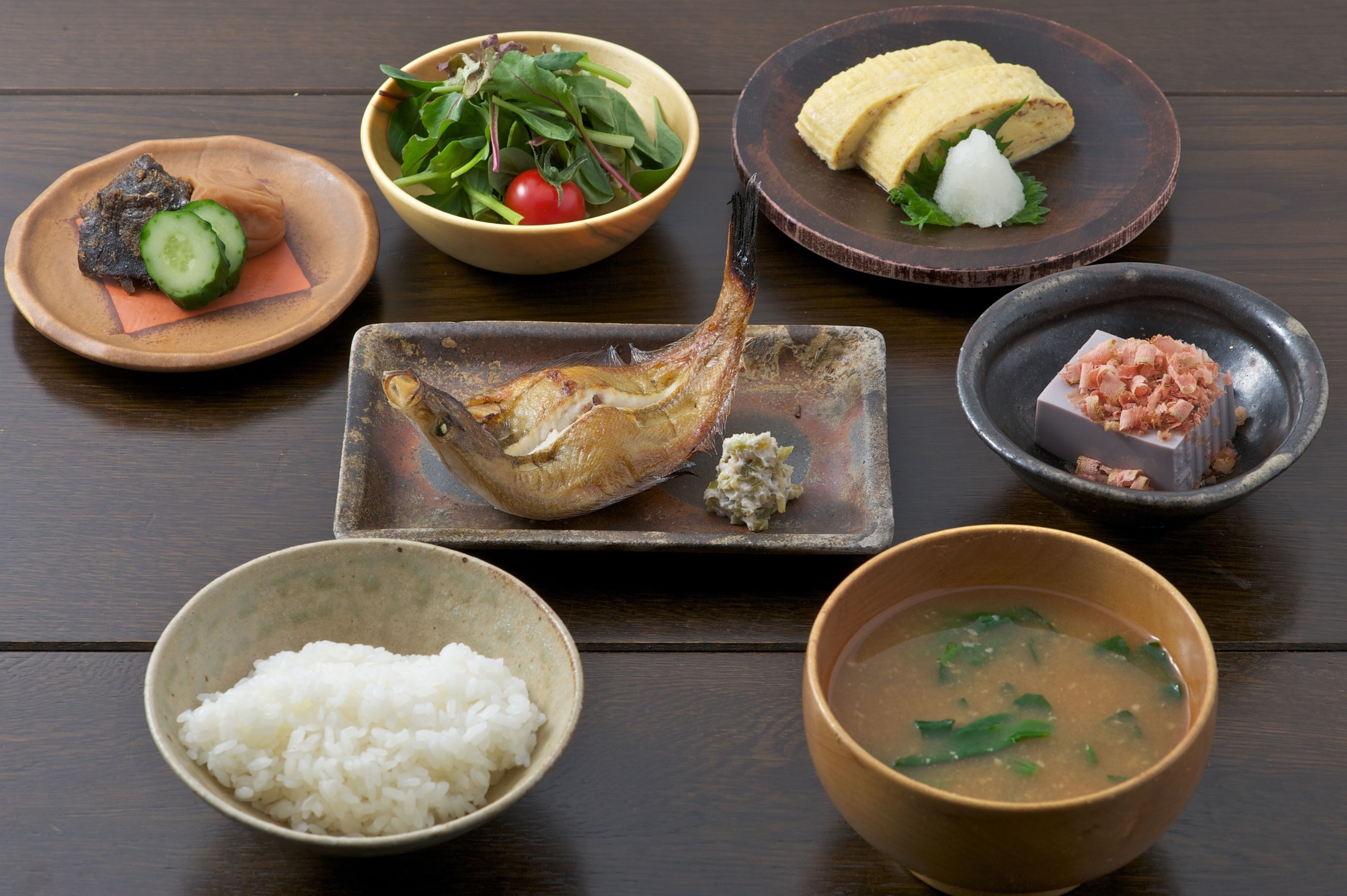 Une variété de plats, notamment du poisson, du riz et de la soupe, disposés sur une table en bois.