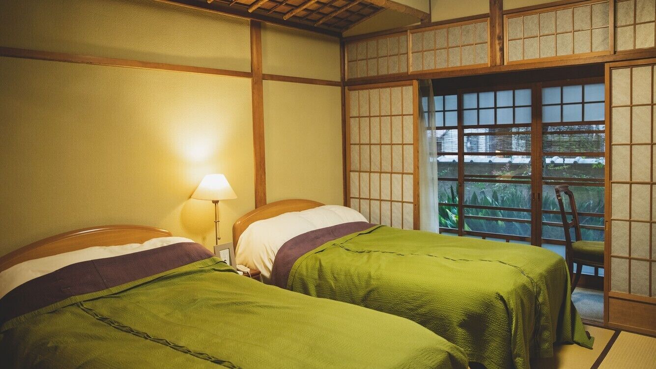 Una habitación tradicional japonesa con suelo de tatami, un biombo shoji y dos camas con ropa de cama verde.