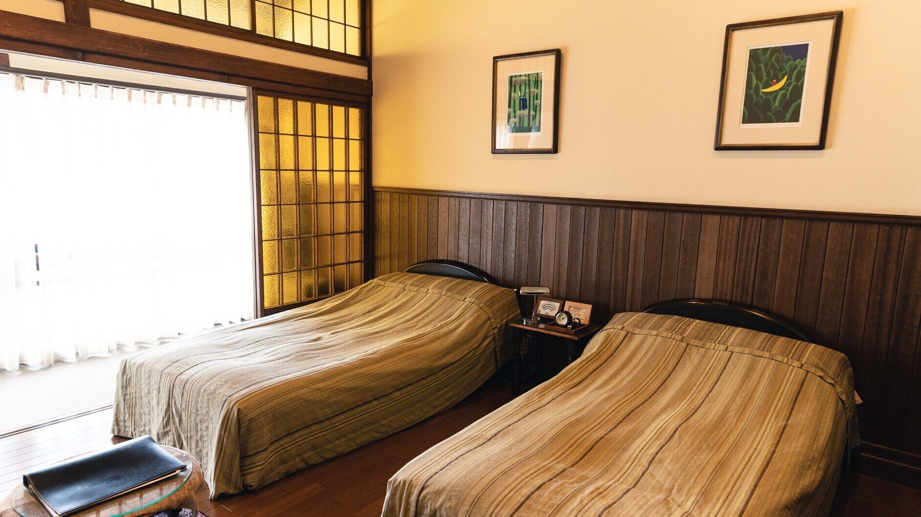 Una habitación con dos camas, una mesita y una mesita de noche con lámpara y reloj.