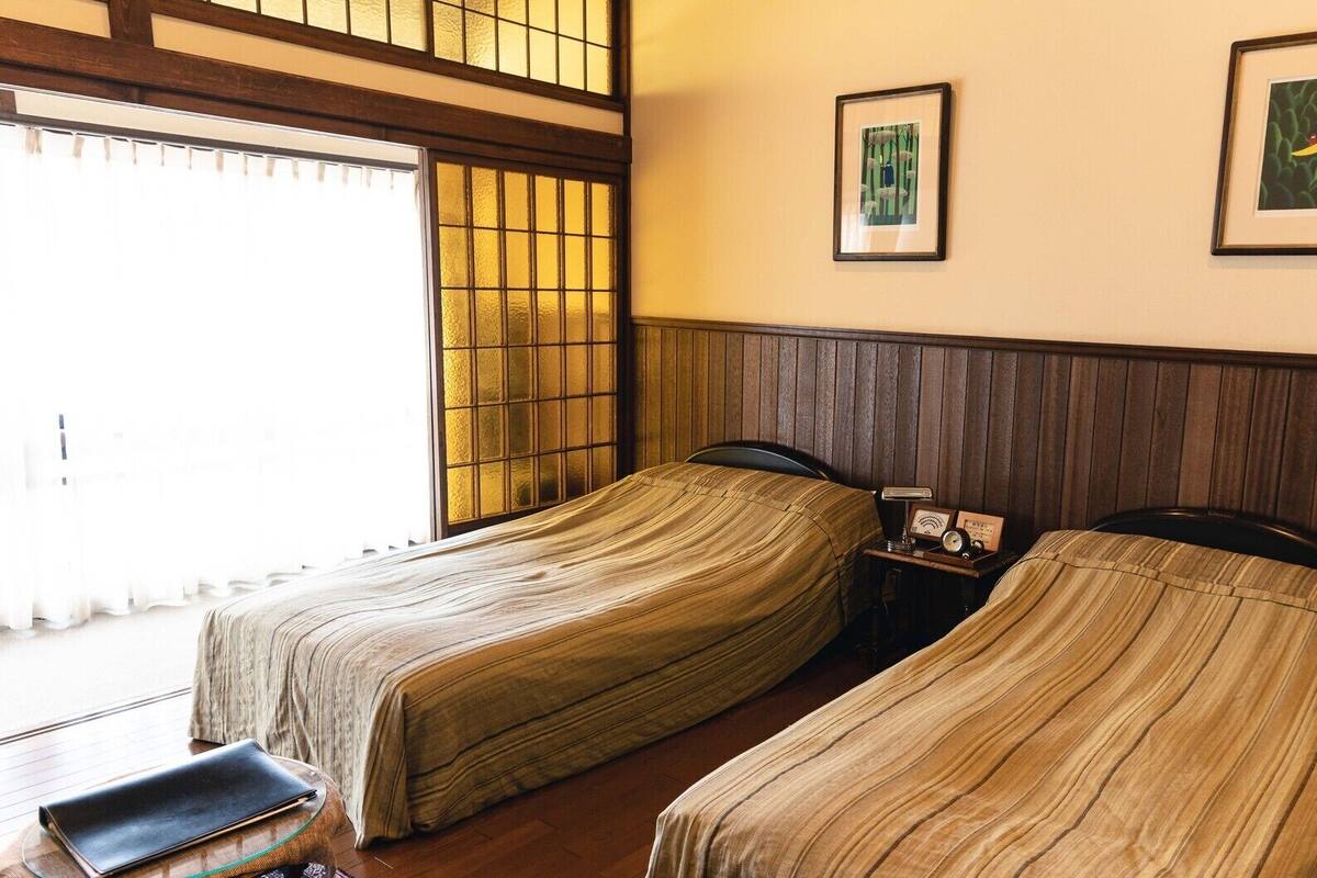 Una habitación con dos camas, una mesita y una mesita de noche con lámpara y reloj.