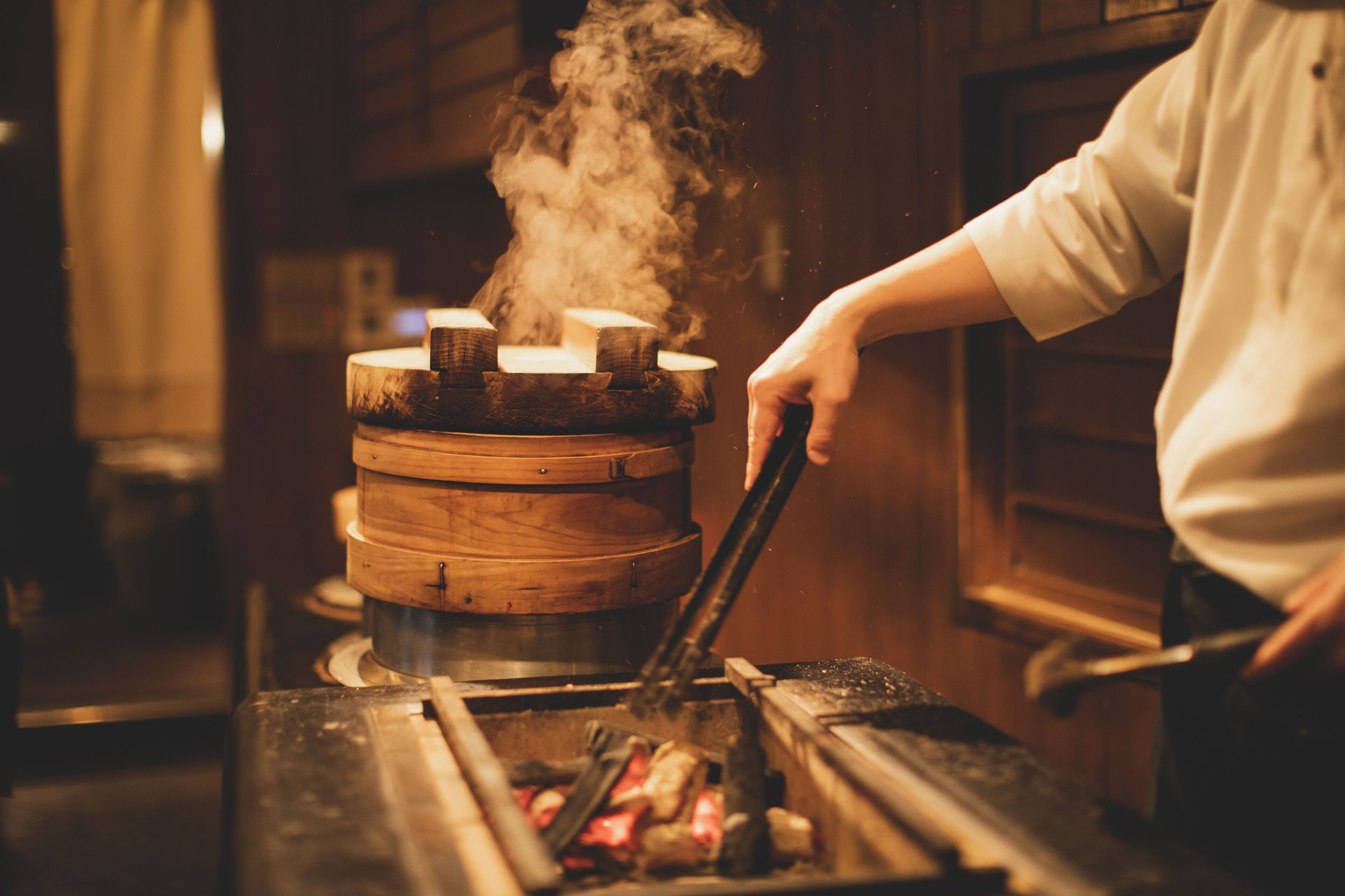 A person cooking with a large wooden stove emitting steam.