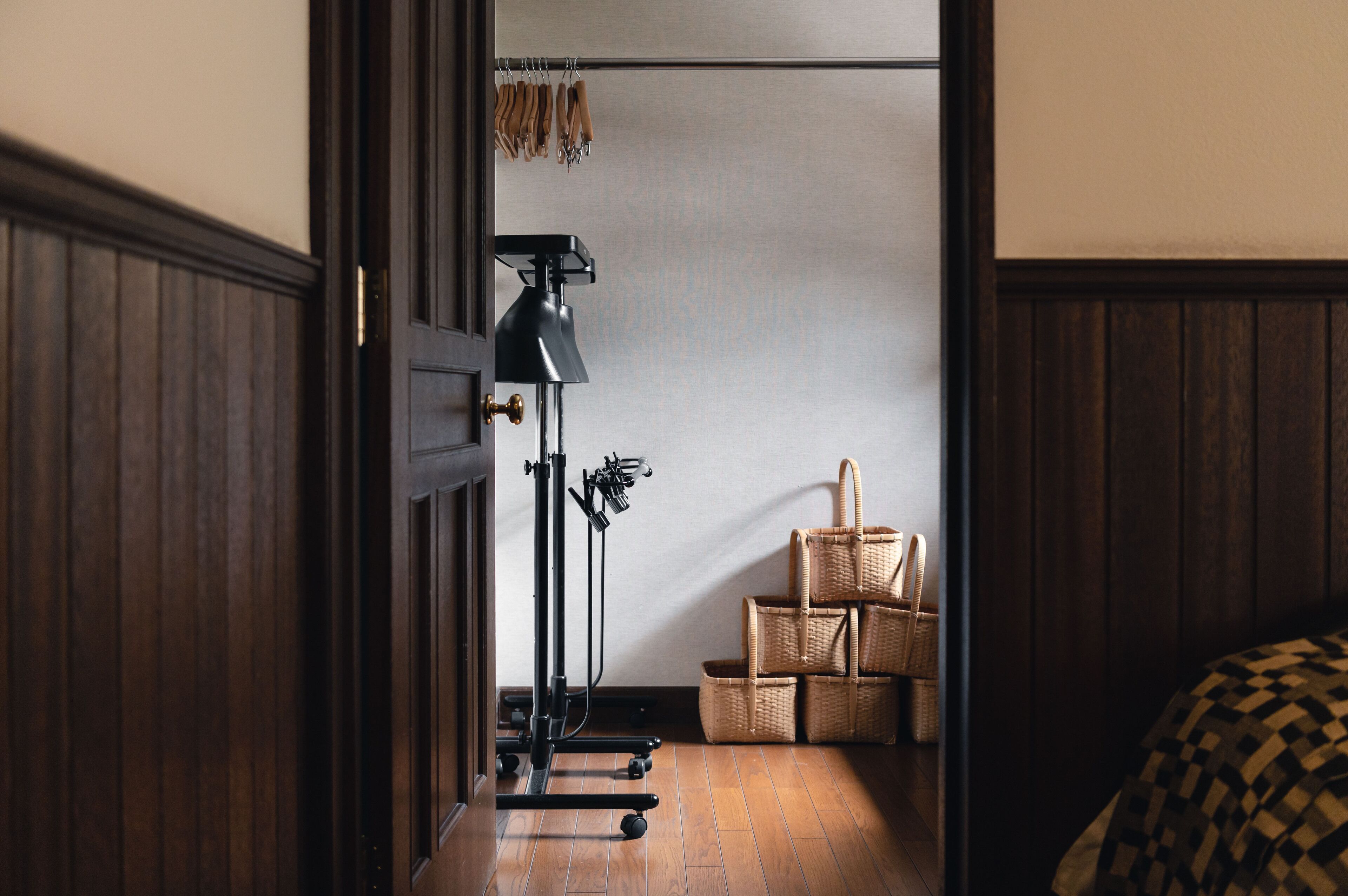 Una habitación con suelo de madera, una lámpara de escritorio negra y una pila de cestas de mimbre.