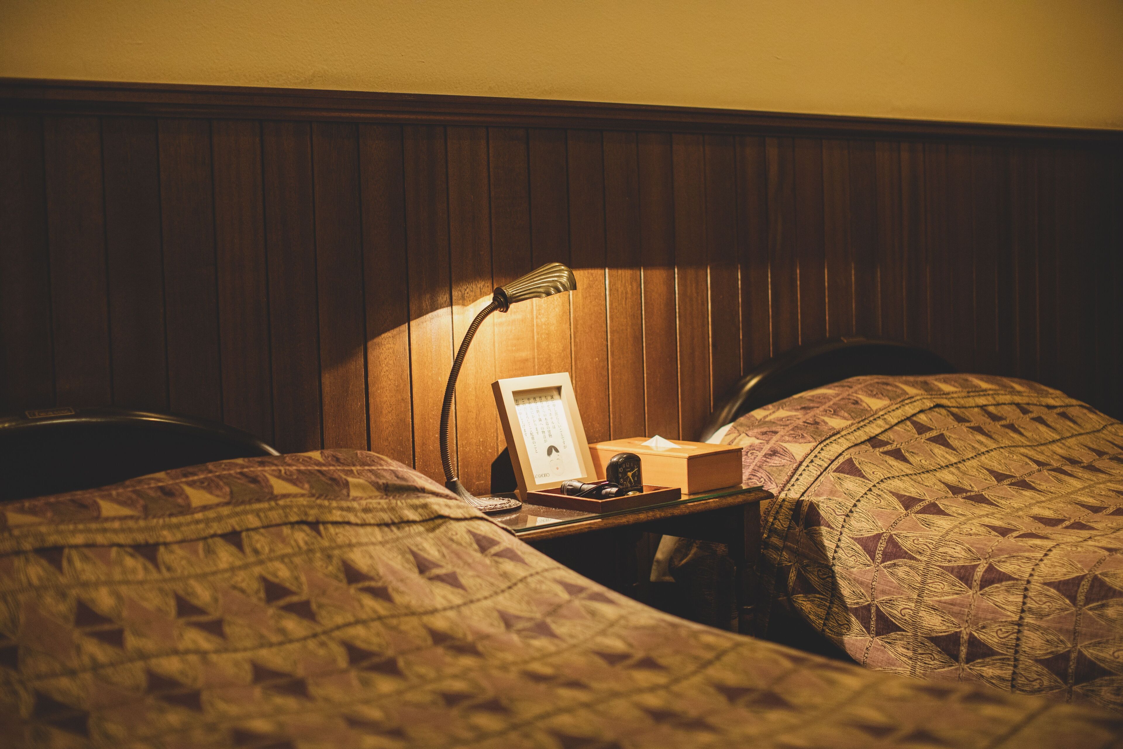 A neatly made bed with patterned bedding, a bedside table with a lamp, a framed picture, and a small clock.