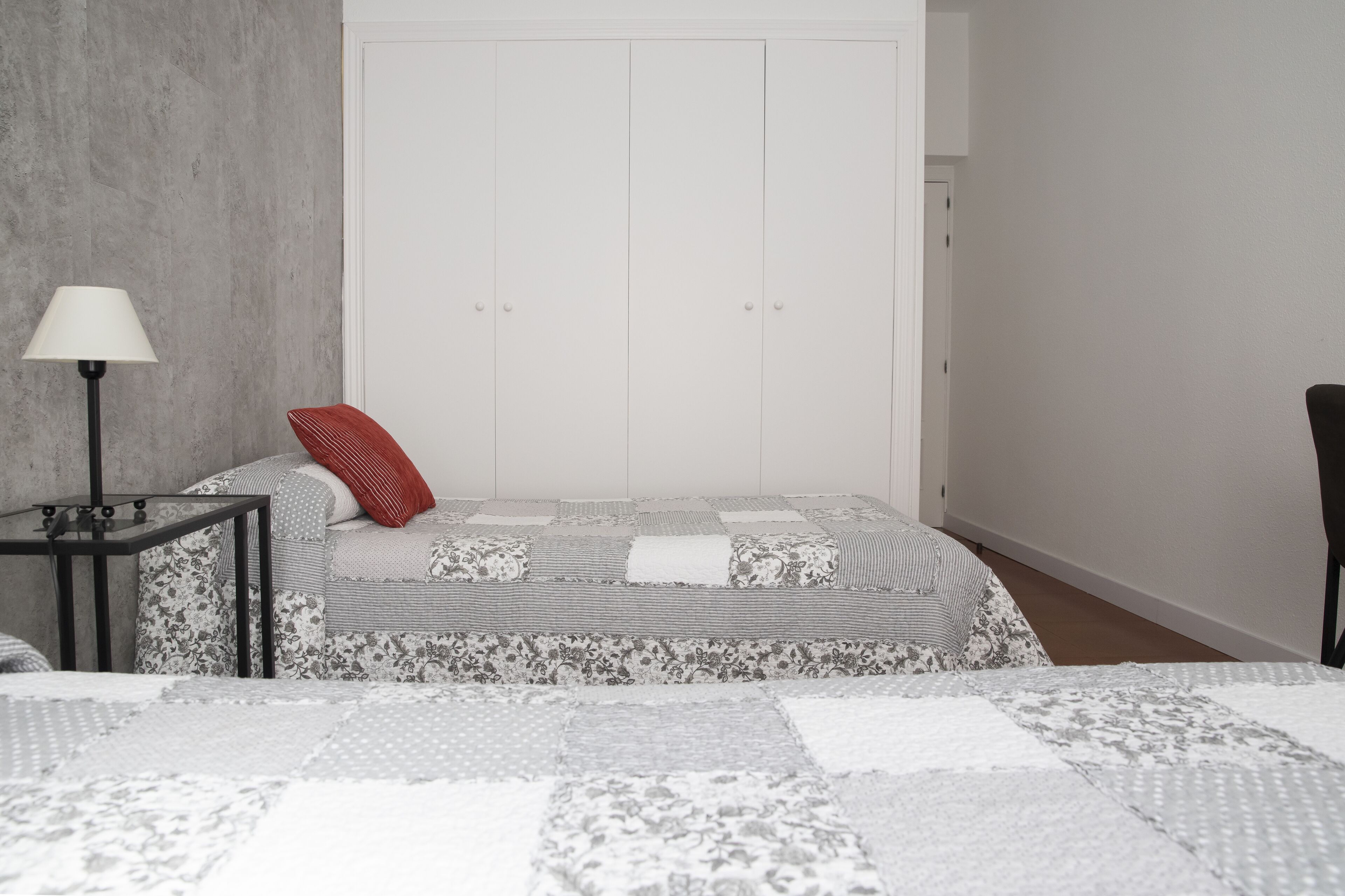A bedroom with a bed, a nightstand, a lamp, and a wardrobe.