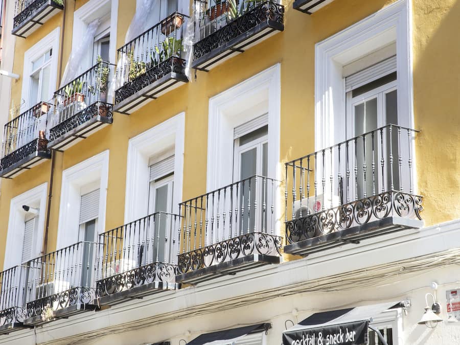 Um edifício com vários andares, varandas, persianas brancas e um letreiro para bar de cocktails e petiscos.