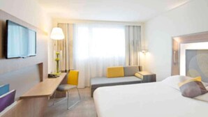 A hotel room with a bed, a desk, a chair, a TV, and a window with curtains. - Novotel Lodz Centrum (Lodz)