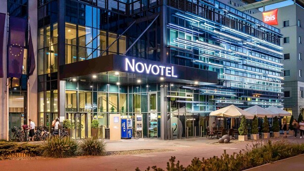 A modern hotel with a glass facade, labeled "NOVOTEL," featuring a prominent entrance and outdoor seating area. - Novotel Lodz Centrum (Lodz)
