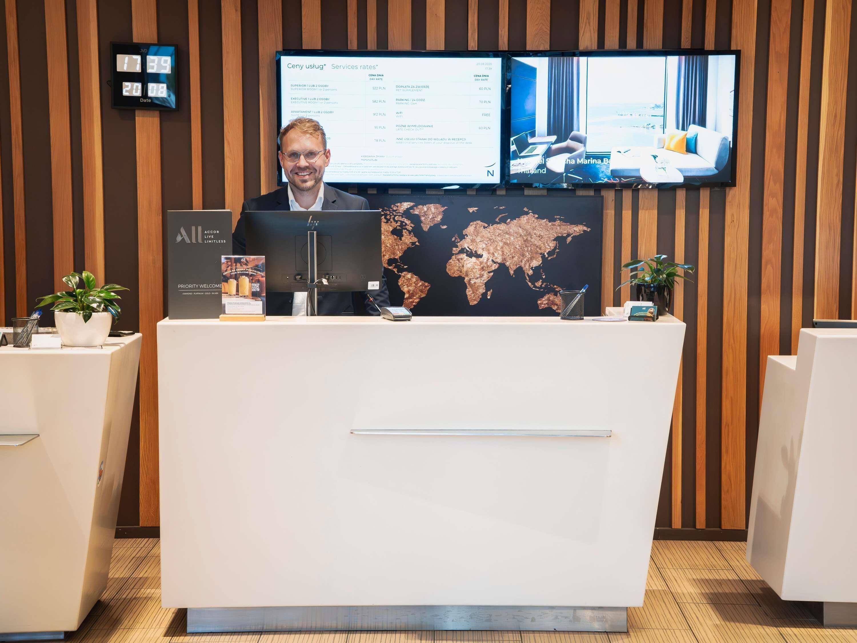 A hotel reception desk with a digital clock, a world map, and a TV displaying services rates.