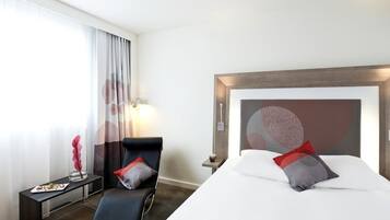 A hotel room with a bed, a chair, a small table, and a lamp.