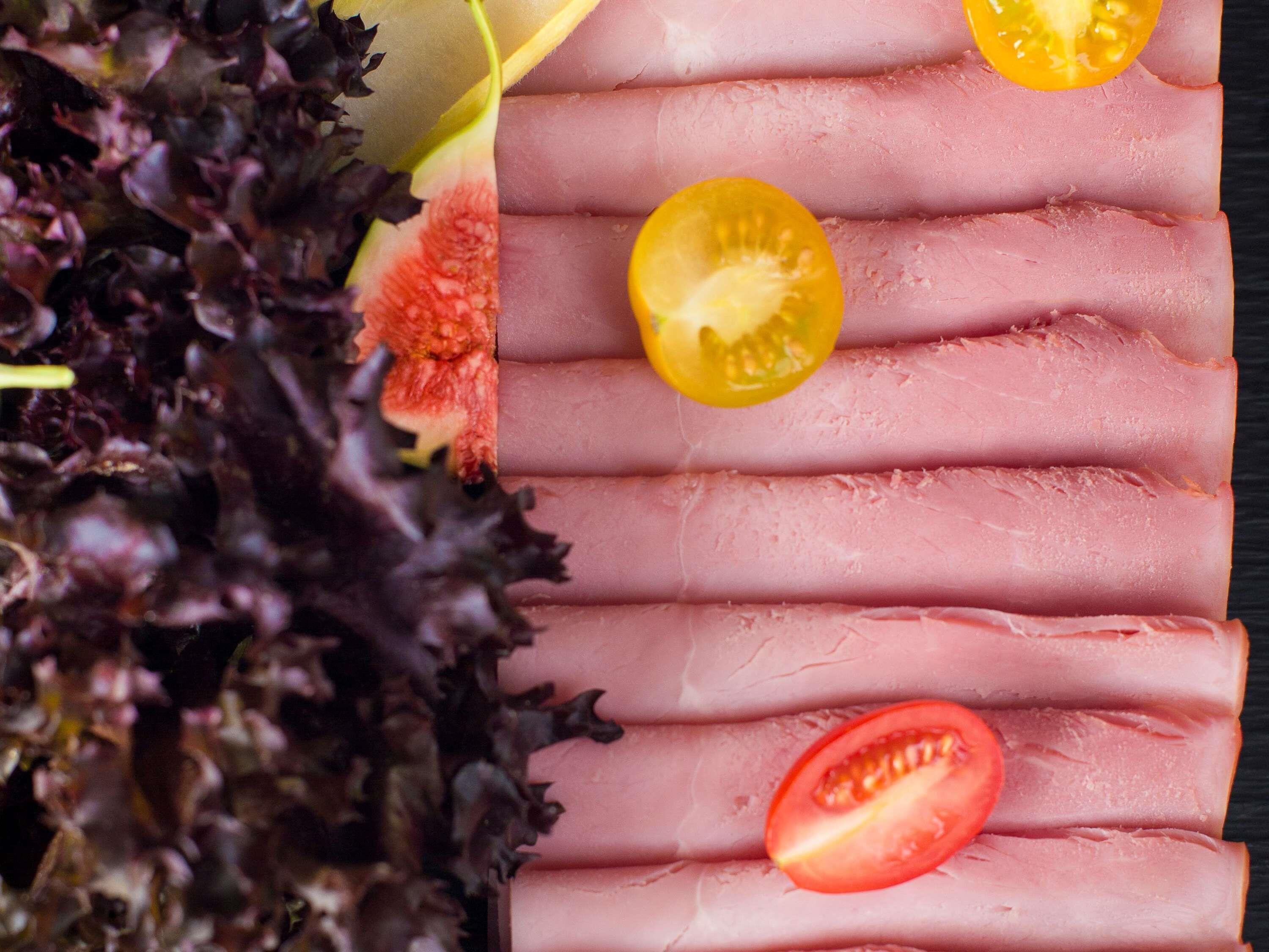 A close-up of sliced ham with cherry tomatoes on a dark background.