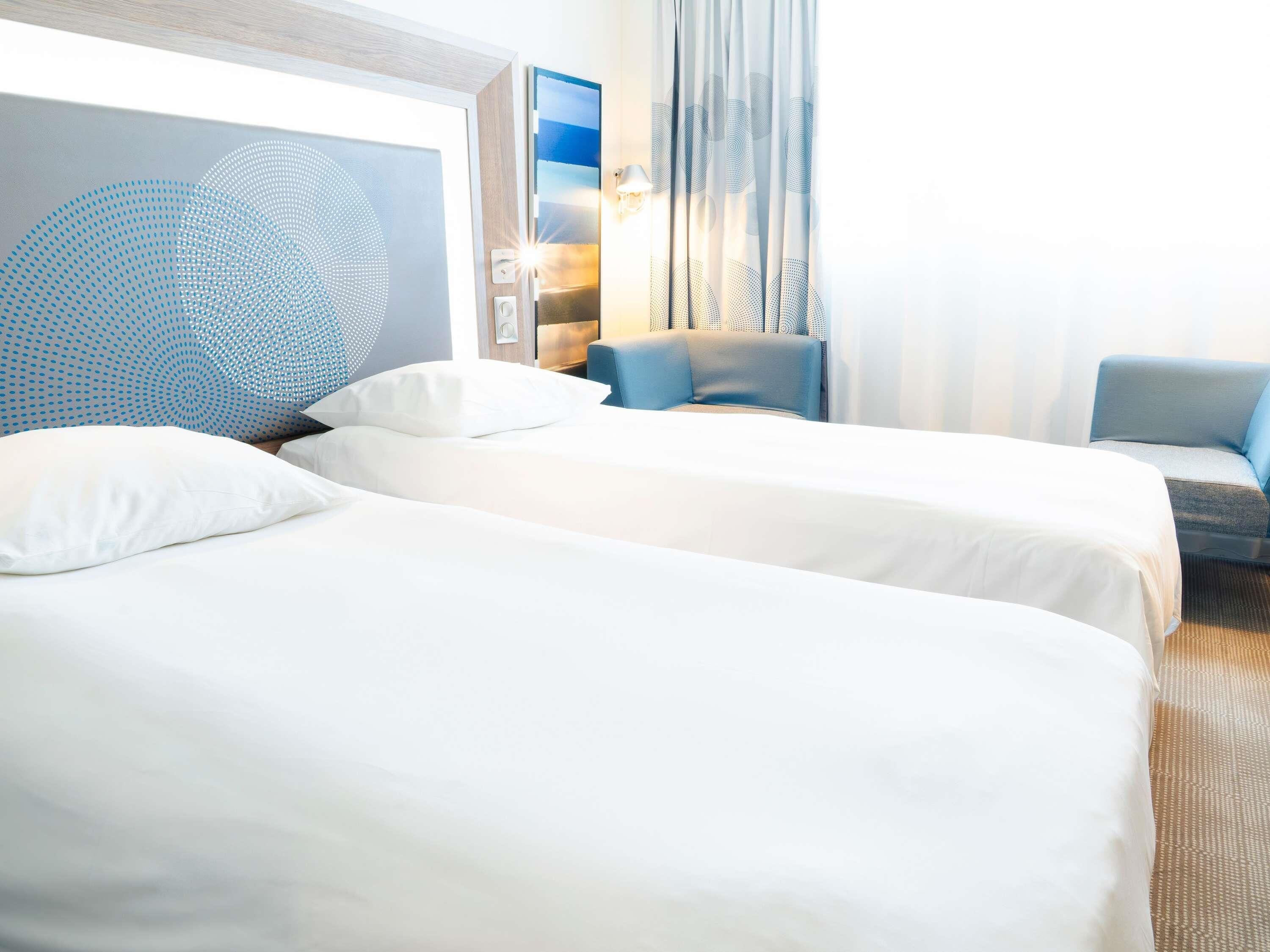 Hotellihuone, jossa on kaksi sänkyä, sohva, televisio ja suuri ikkuna.
