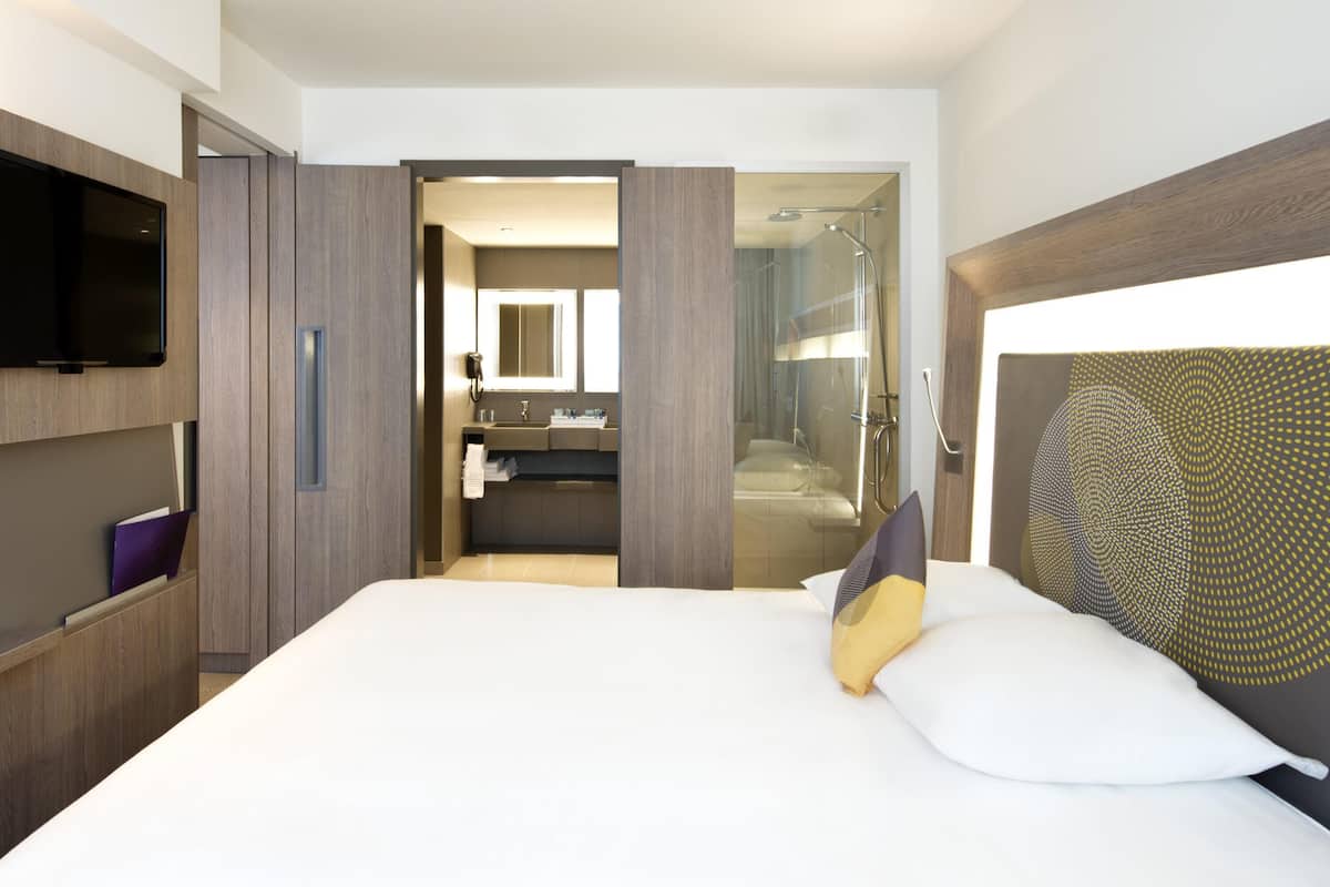 Ein modernes Hotelzimmer mit einem großen Bett, einem Fernseher, einem Badezimmer mit Dusche und einem begehbaren Kleiderschrank.
