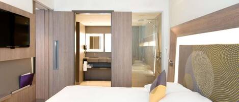 Una habitación de hotel con cama, televisión, baño con ducha y espejo.