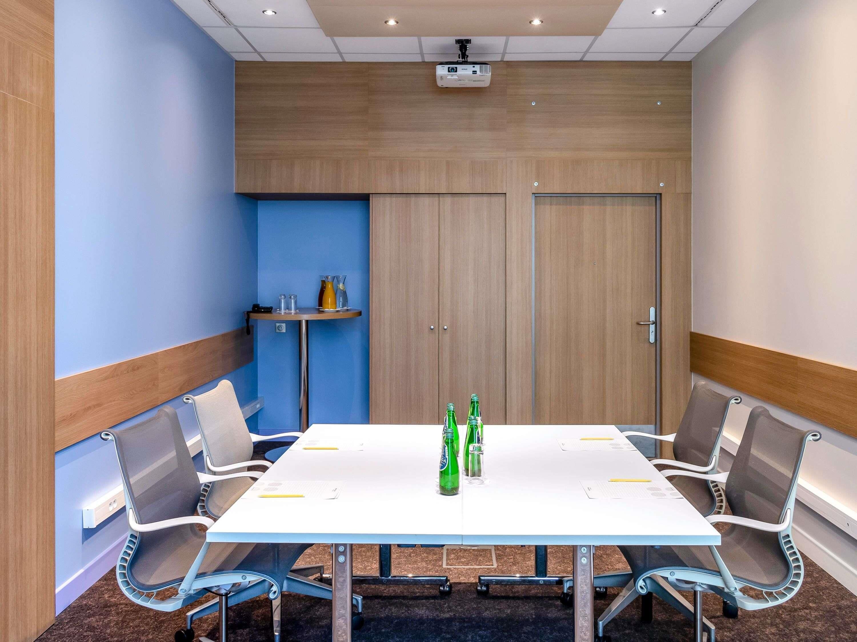 A conference room with a white table, six chairs, a projector, and a blue accent wall.