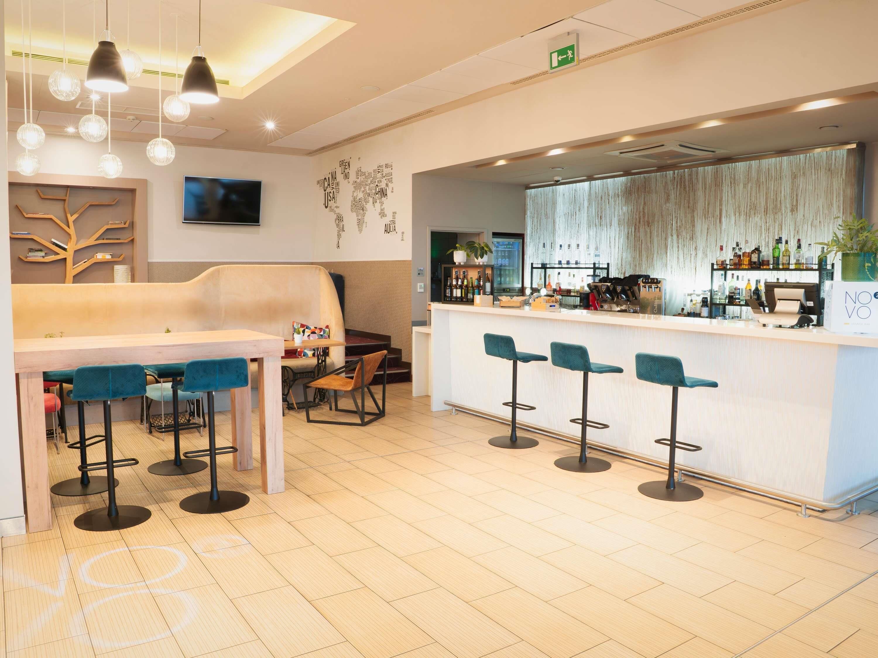 Un área de bar moderna con mostrador de madera, taburetes y un espacio de estar con sofá y sillas.