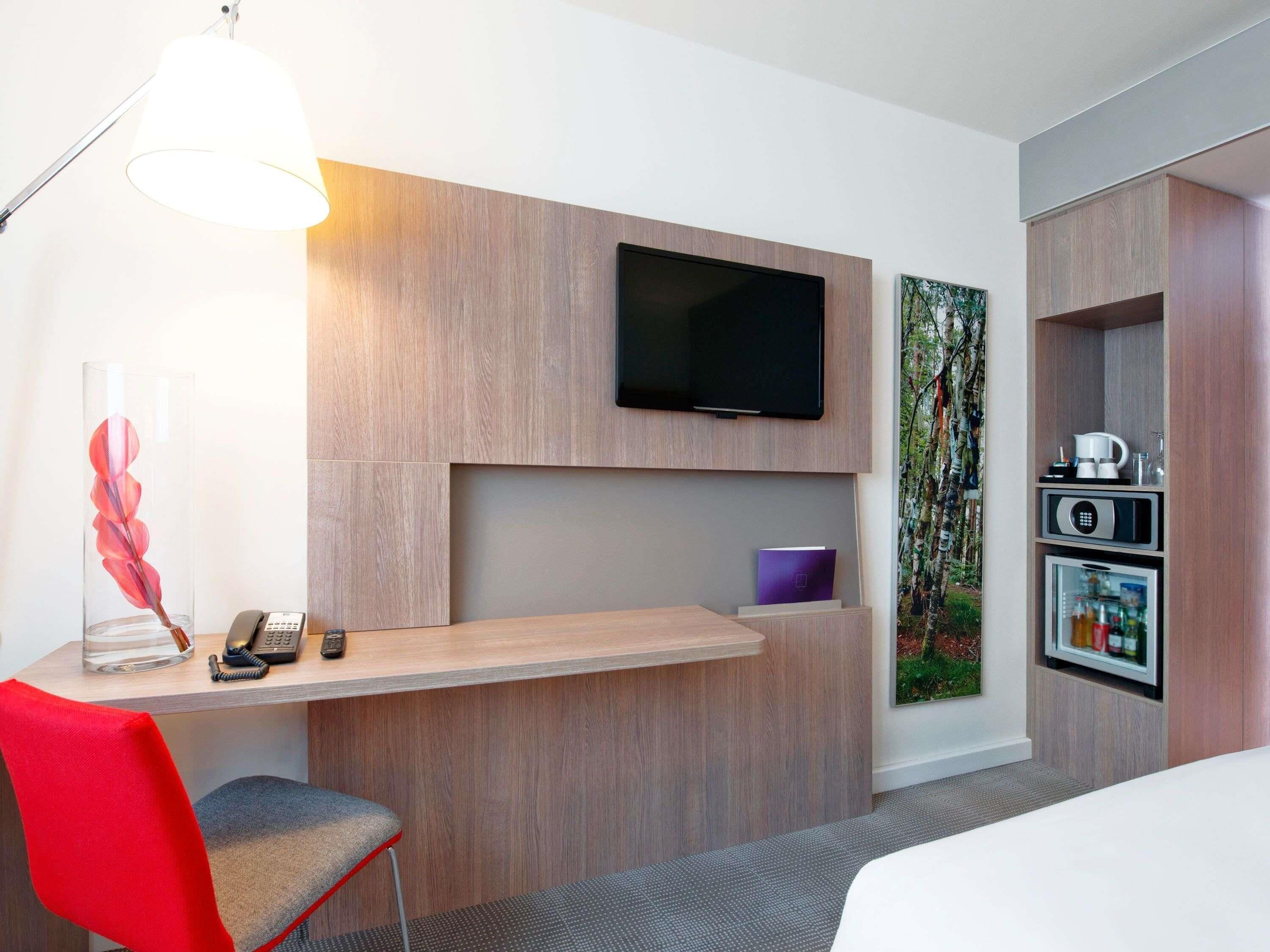 Habitación de hotel con escritorio, silla, televisor y minibar incorporado.