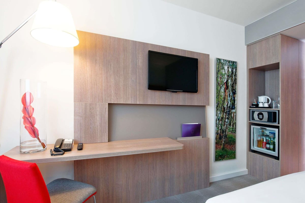 Habitación de hotel con escritorio, silla, televisor y minibar incorporado.