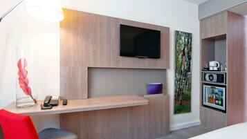 Habitación de hotel con escritorio, silla, televisor y minibar incorporado.
