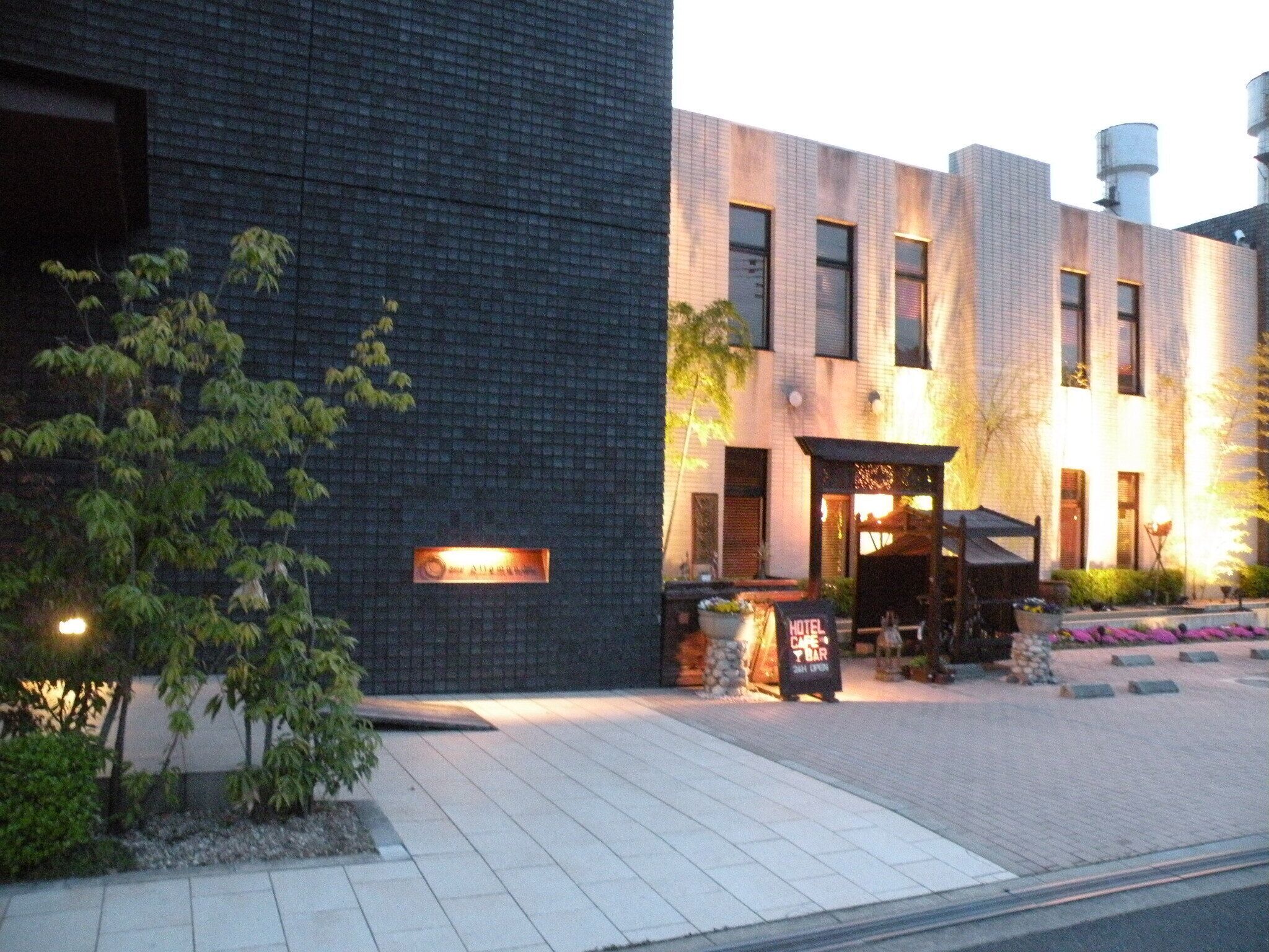 A modern hotel with a brick facade, a cafe bar, and a sign indicating it is open 24 hours.