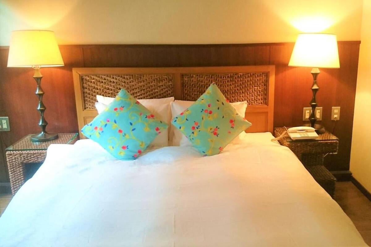 A hotel room with a large bed, two bedside lamps, a nightstand with a phone, and a wooden headboard.