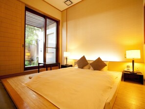 A hotel room with a large bed, two bedside lamps, and a view of greenery through a sliding door. - Hotel Allamanda (Nara)