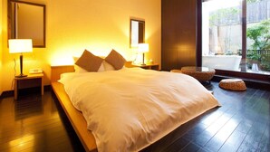 A hotel room with a large bed, two bedside tables with lamps, a large window with a view of greenery, and a dark wooden floor. - Hotel Allamanda (Nara)