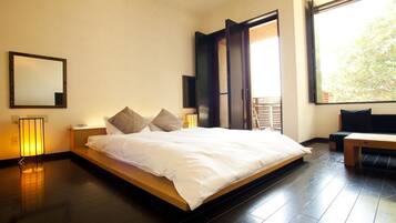 A modern bedroom with a large bed, bedside lamps, a mirror, and a view of the outdoors.