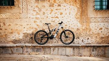 Un vélo tout-terrain est garé contre un mur de pierre à la texture particulière, près d’une fenêtre et d’une porte.