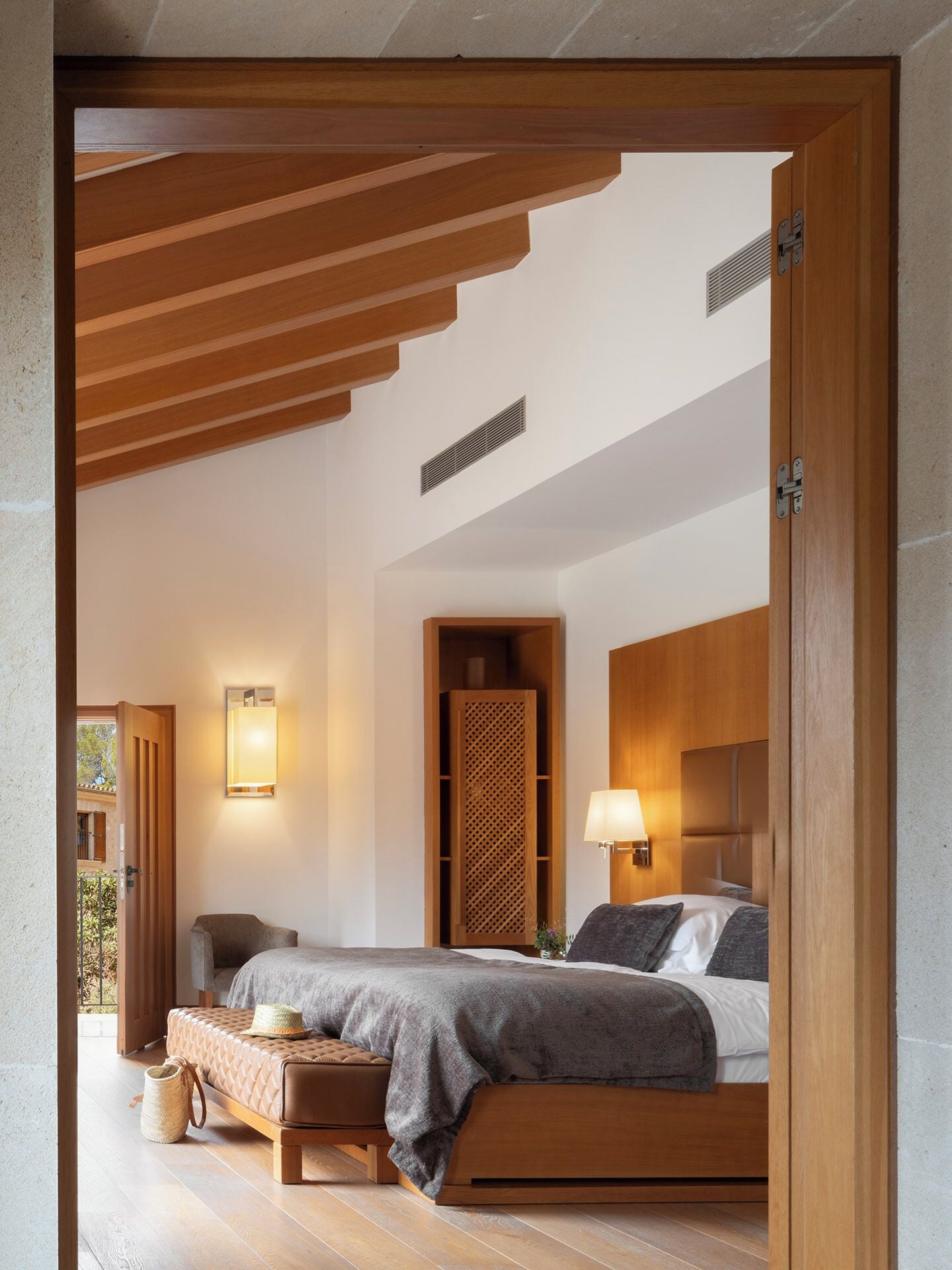 Une chambre à coucher moderne avec un lit en bois, un banc et une lampe fixée au mur.