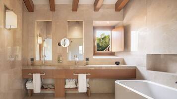 A modern bathroom with a large bathtub, a double vanity with two sinks, and a large mirror.