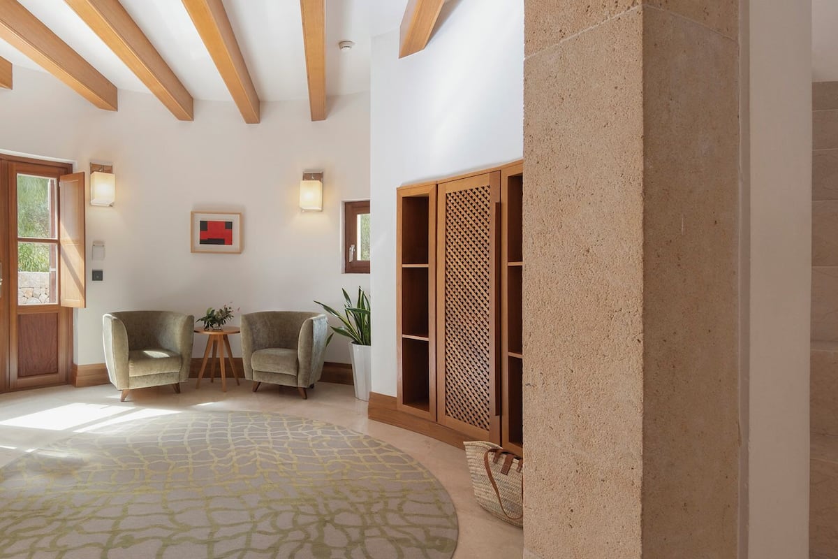 A spacious living area with a large window, two armchairs, a round rug, and a wooden bookshelf.